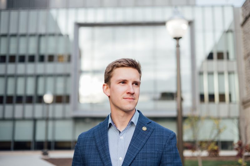 Sam Kennedy, a student veteran in a blue blazer, stands in front of a building on Virginia Tech campus.