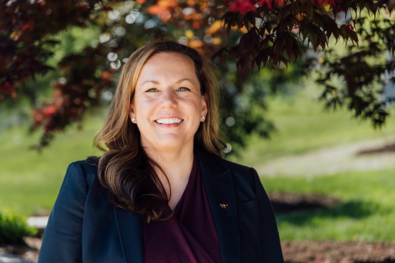 Woman smiling outside in a black jacket and maroon blouse.