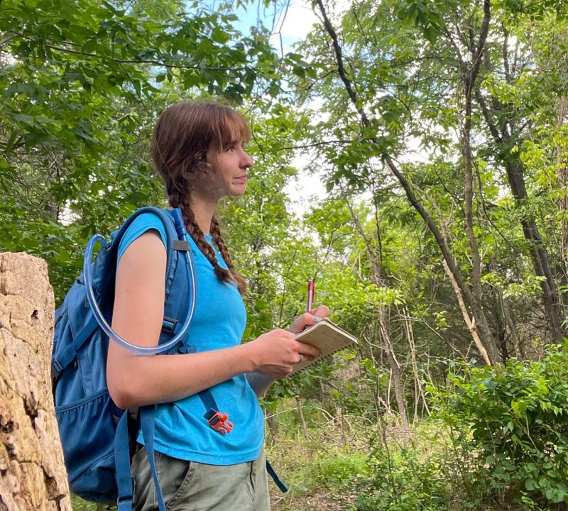 Abby Marino writes in a notebook while in the woods.