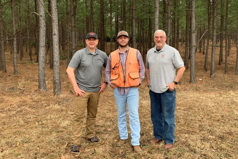 Josh Turner, Caleb Turner, and Dale Turner stand together in front of pine trees