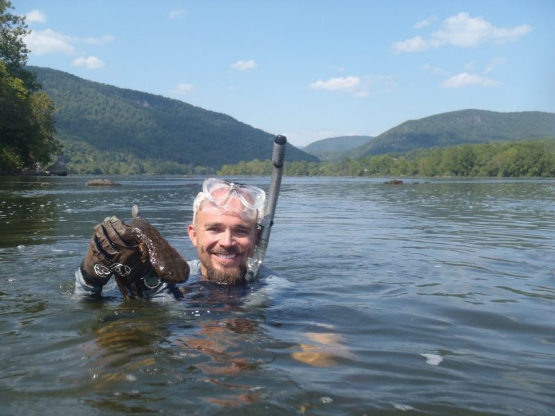 Bill Hopkins  holds a hellbender salamander while scuba diving in the water.