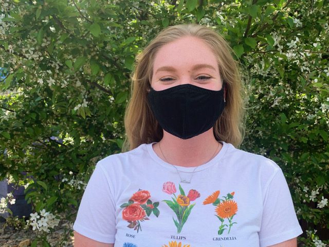 Gwyneth Martin, a senior in marine fish conservation, participated in this year’s Fralin Undergraduate Research Fellowship (FURF) even amidst the COVID-19 pandemic. She is standing in front of a bright green tree with a black mask on and a shirt with flower species on it. Photo courtesy of Gwyneth Martin.